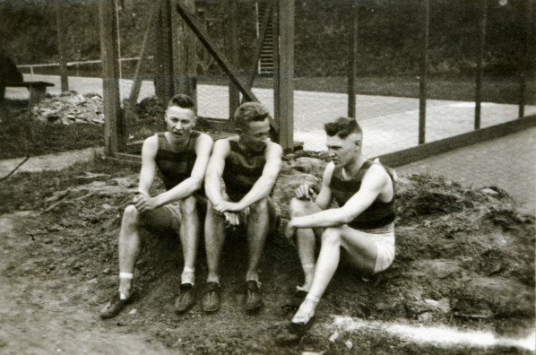	Black and white photo of three unidentified track athletes seated at the side of a track in 1915. 